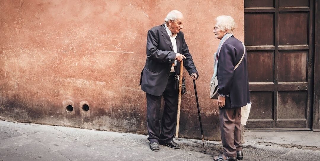 Twee oudere mensen praten buiten, van wie één met een wandelstok